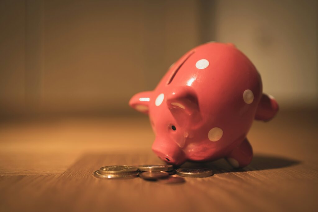 A pink polka-dotted piggy bank on a wooden floor surrounded by coins symbolizing budgeting and saving money for newcomers.