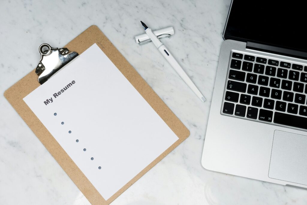 A blank resume sheet on a clipboard next to a white pen and an open laptop on a marble desk, symbolizing job application or resume writing